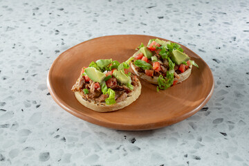 A view of two carnitas sopes, on a plate.