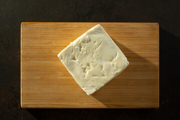 A top down view of a block of feta cheese, on a wood board.