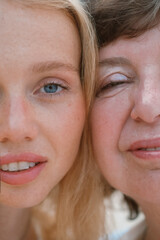 Close up portrait of a young red haired woman and her senior mother standing on the beach by the ocean during their vacation together. Daughter and mother on a trip. Mothers day.