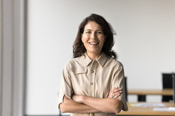 Mature professional woman standing confidently in office with her arms crossed, look at cam....