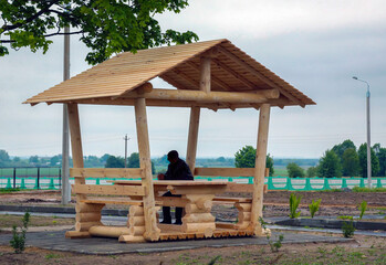A person resting under a wooden gazebo in a peaceful rural setting on an overcast day
