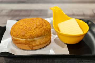 A close-up view of a polo bun with butter. The bun's outer layer is cracked and crunchy, offering a...