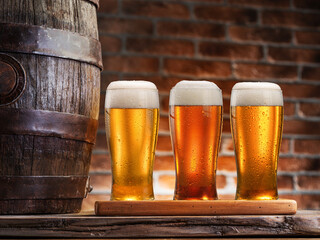 Three glasses of chilled beer on old wooden table and brick wall at the background.