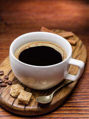 Cup of coffee on white plate, several coffee beans and brown sugar on wooden table close up. Top view.