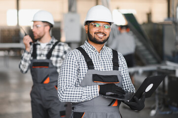Portrait of Indian male engineer into the factory while his hand is holding the laptop
