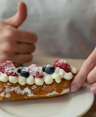Person is holding a pastry with strawberries and blueberries on top