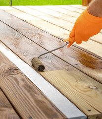 Man is painting a wooden deck with a roller