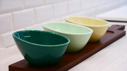 Close-up of colored porcelain bowls on a wooden board on the kitchen table