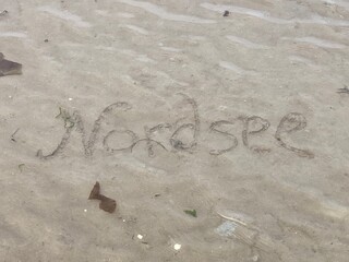 Schriftzug Nordsee wird bei Flut überspült mit Wasser