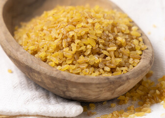 Raw dry uncooked yellow bulgur grain in a wooden bowl on white table cloesup. Ancient food