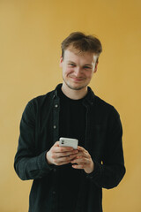 Young Smiling Man Using Smartphone Against Yellow Background