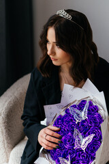 A stunning young woman with a tiara and an elegant black coat holds a luxurious bouquet of vibrant...