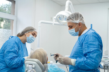  male dentist surgeon in uniform with assistant doing operation for install dental implant teeth of...