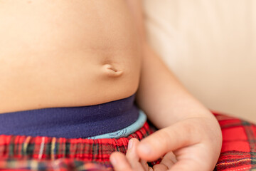 Child relaxing indoors wearing plaid pants and blue waistband while showing a close-up of their...