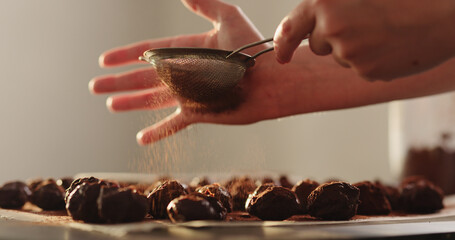 young woman sprinkle cocoa powder on chocolate truffles
