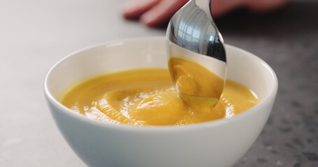 Eating pumpkin cream soup in a white bowl on concrete backdrop