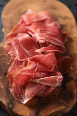 Sliced prosciutto ham on olive wood board