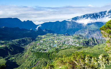 Naklejka premium Scenic aerial view of Cilaos, French Reunion Island, surrounded by lush green mountains, rugged peaks, and clouds, showcasing a breathtaking landscape