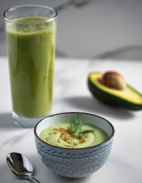 Bol de sopa fr&iacute;a de aguacate y pepino, decorado con eneldo y especias, acompa&ntilde;ado de batido verde.