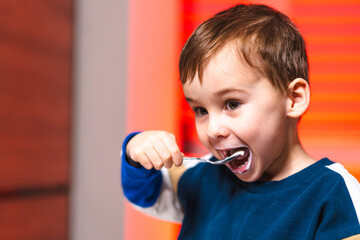 Boy savoring chocolate dessert. A cheerful young boy smiles as he takes a bite of chocolate dessert with a spoon, feeling happy at home.