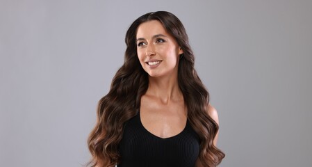 Naklejka premium Hair styling. Beautiful woman with wavy long hair on grey background