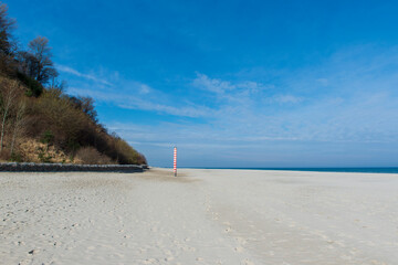 Sandy Beach with Cliffs and a Striped Navigation Pole Under a Clear Blue Sky in Jastrzębia Góra