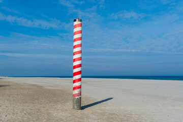 Striped Navigation Pole on a Sandy Beach with Blue Sky and Sea in Jastrzębia Góra