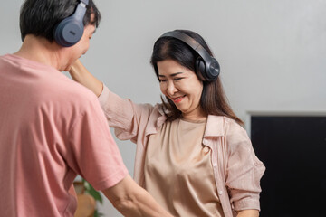 Mature couple joyfully dancing at home with headphones, enjoying music.