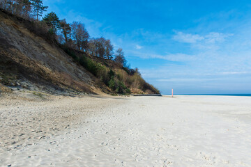 Sandy Beach with Cliffs and a Striped Navigation Pole Under a Clear Blue Sky in Jastrzębia Góra