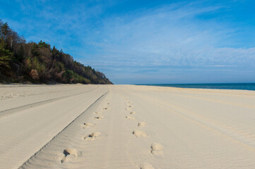 Tire Tracks and Footprints on a Vast Sandy Beach with Cliffs and Blue Sky in Jastrzębia Góra