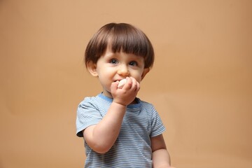 Cute little child eating tasty mochi on light brown background