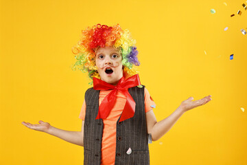 Surprised boy dressed like clown and flying confetti on orange background. Surprise party