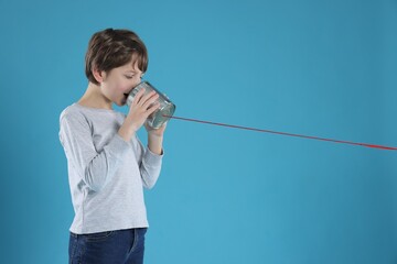 Boy using tin can telephone on blue background