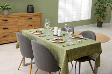 Stylish table setting with olive tablecloth, glasses and candles in dining room