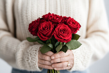 Delicate hands gently hold a bouquet of vibrant red roses, beautifully contrasting with the cozy cream sweater. The intimate moment radiates warmth, love, and appreciation.