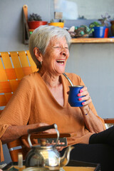 portrait of laughing senior latino woman drinking mate in her patio