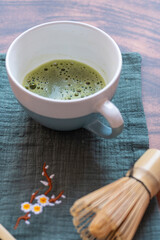 Cup of matcha tea with bamboo whisk on placemat