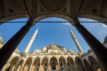 Fototapeta premium Low angle view of Suleymaniye Mosque main dome and minarets framed by courtyard arches against a blue sky, Istanbul, Turkey