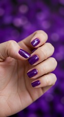 Elegant purple manicure on hand against blurred violet background