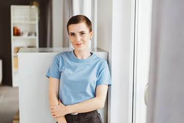 Confident Young Woman in Blue T-Shirt Standing by Window