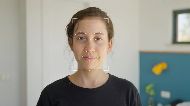 Face detection and identification technology applied on female looking at camera. Young woman standing in room with AI algorithm methods recognizing facial features scan capture for human similarity