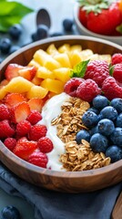 A wooden bowl filled with yogurt, granola, blueberries, raspberries, pineapple and strawberries.  Close-up shot of a healthy breakfast or snack.