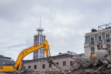 Yellow excavator working on demolition site in urban area. Heavy machinery operating on...
