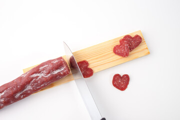 Heart-shaped slices of salami on a wooden board with a knife, ideal for showcasing themed food ideas, catering services, or Valentine Day promotions. A fun and unique twist on a classic snack
