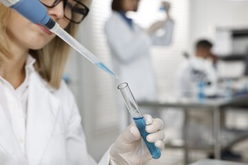 Scientist with micropipette and test tube working in laboratory, closeup