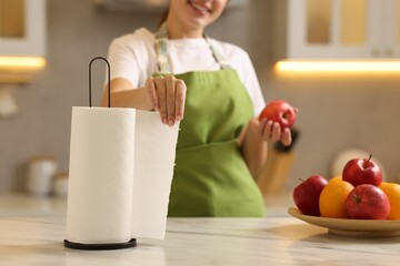 Woman with apple using paper towels at white marble in kitchen, closeup