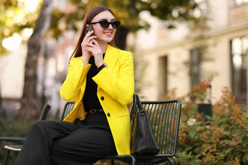 Fototapeta premium Smiling businesswoman in stylish suit talking on smartphone outdoors
