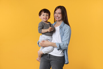 Happy mother with her cute little son on yellow background