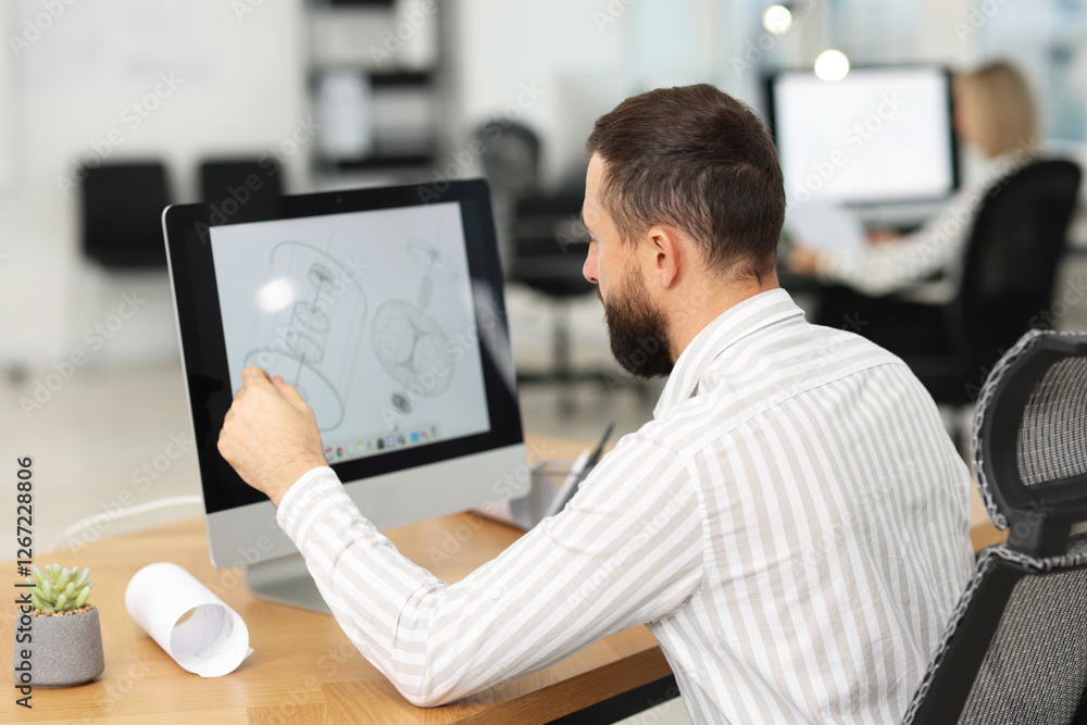 Poster technician making digital engineering drawing on computer at desk in office