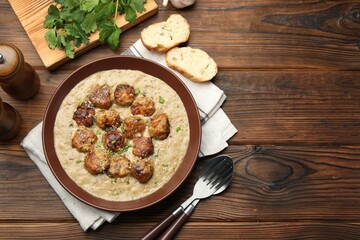 Delicious meatballs with gravy cream sauce and herbs served on wooden table, flat lay. Space for text